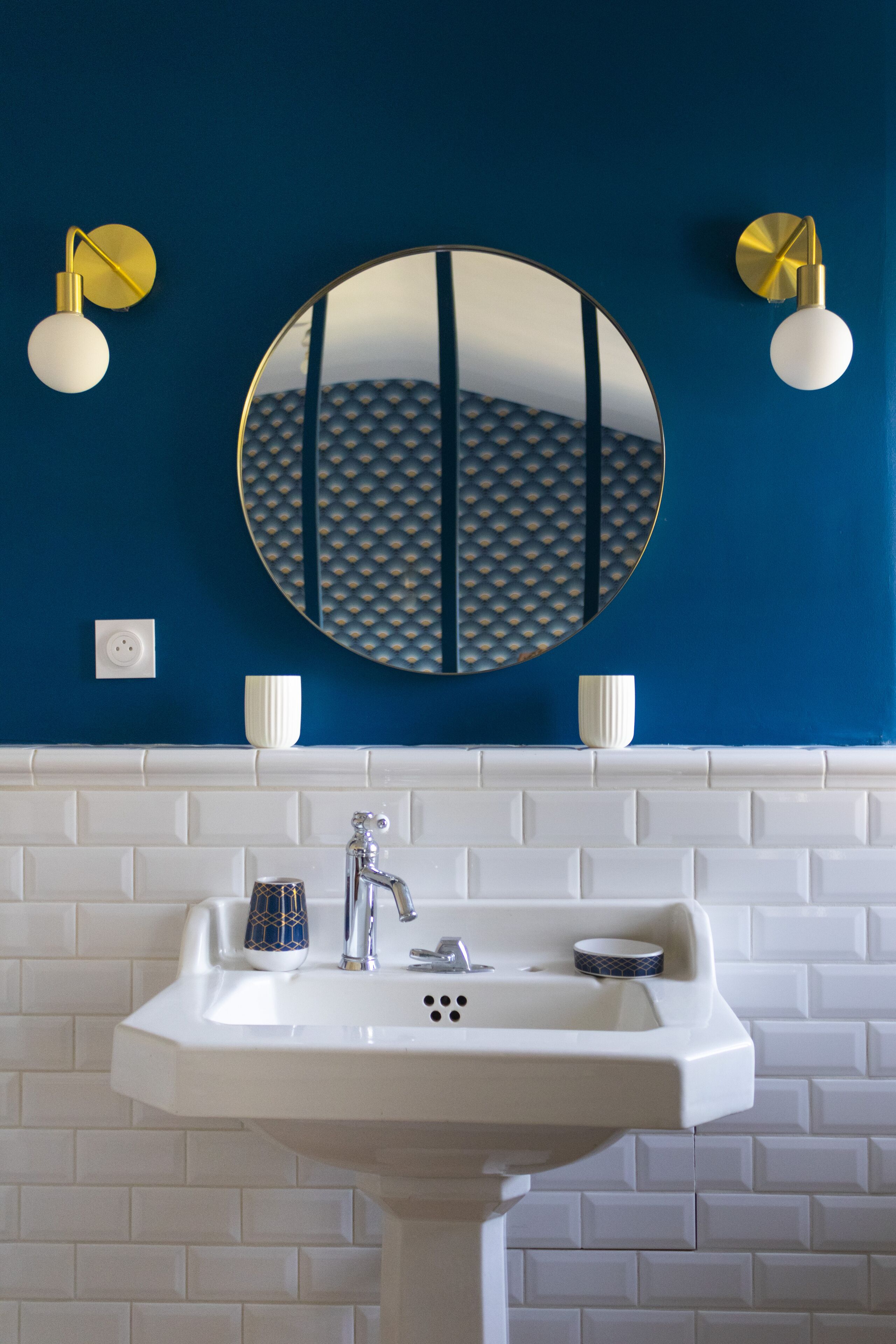 A bathroom with a white sink, a round mirror, and two wall-mounted lights.