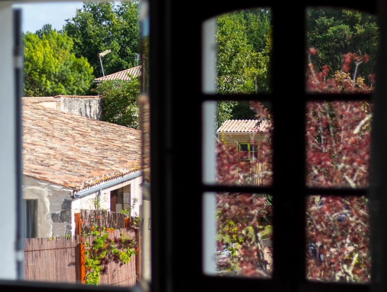 Vista attraverso una finestra di un edificio rustico con tetto in tegole e recinzione in legno.