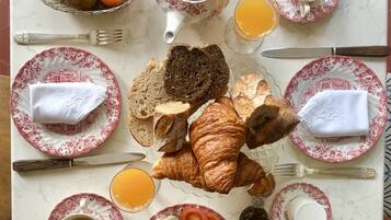 Une table de petit-déjeuner avec des croissants, du pain, du fromage, des tomates et un panier de fruits.