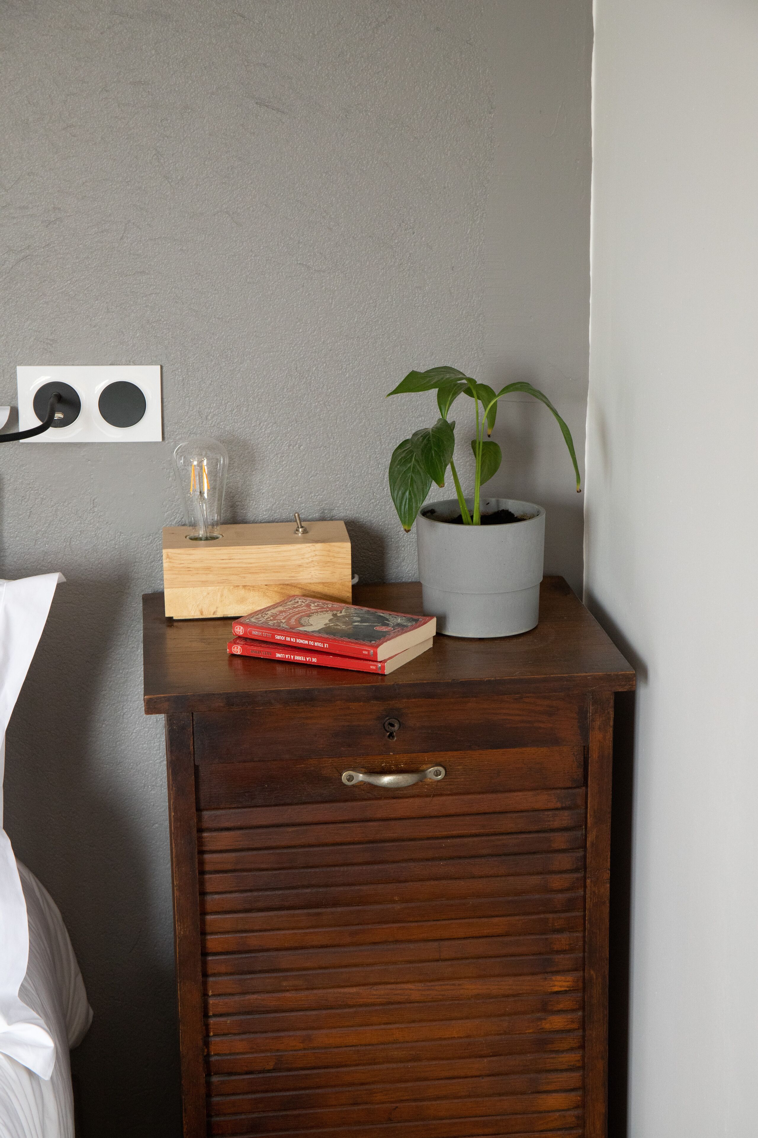 A wooden nightstand with a potted plant, a glass vase, and a few books.