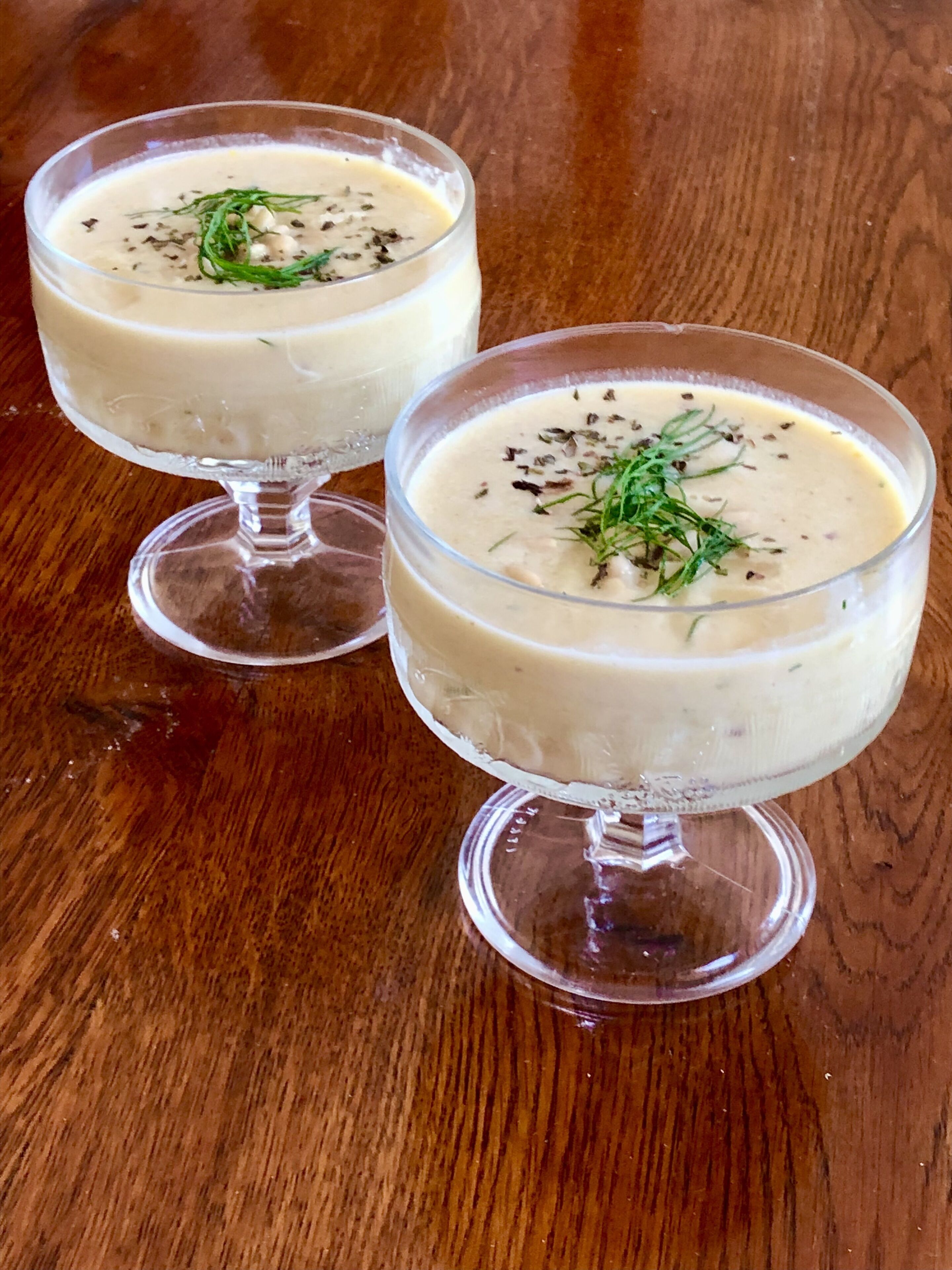 Deux bols de soupe crémeuse, garnis d’herbes, sur une table en bois.