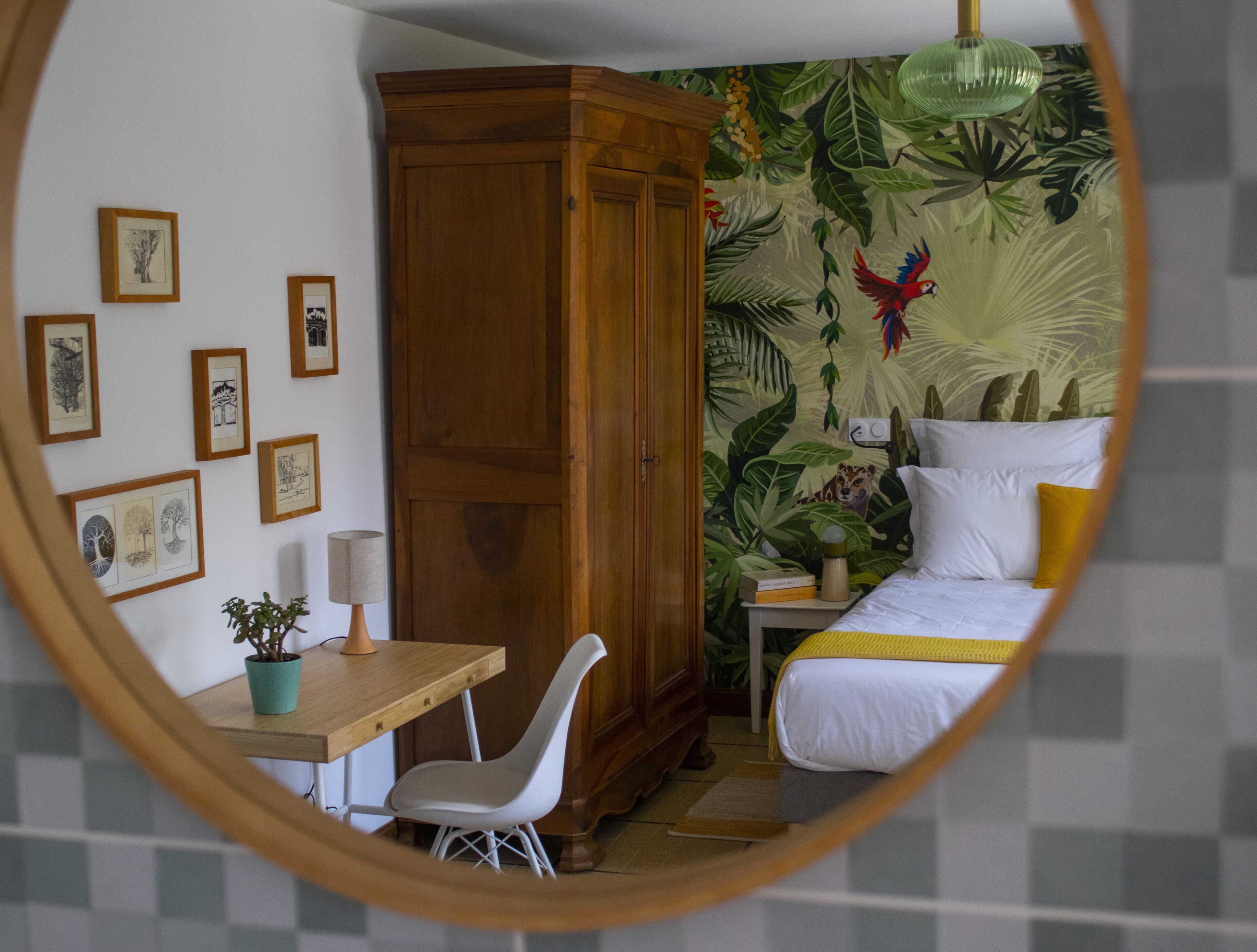 Een slaapkamer met een bed, een houten garderobe, een bureau met stoel en een wand met ingelijste foto's.