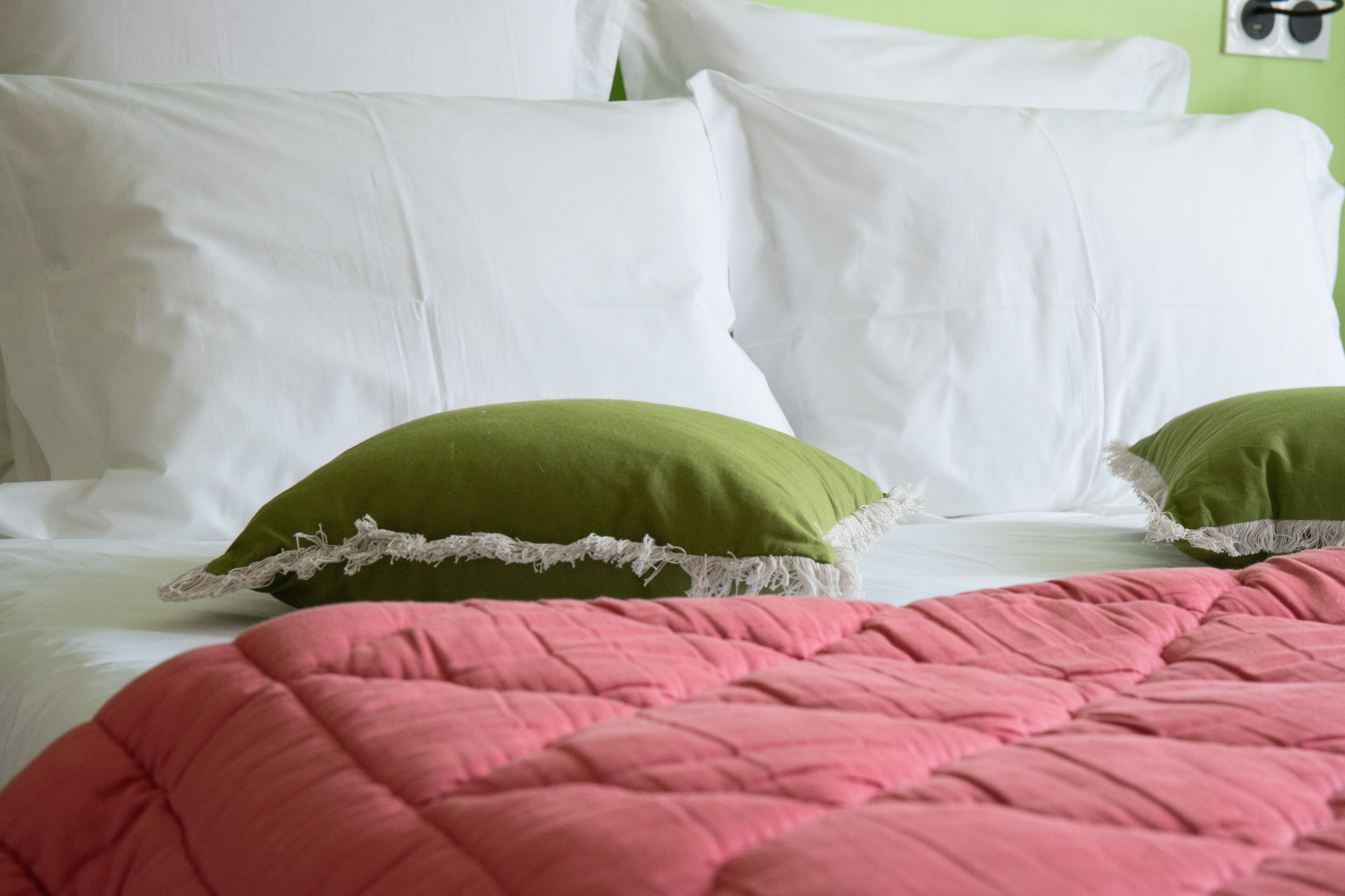 Een bed met witte en groene kussens, een roze sprei en een groene muur.