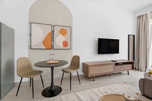 A modern living room with a round table, two chairs, a flat-screen TV, and a wooden cabinet. - Silkhaus Luma21, JVC Dubai (Dubai)
