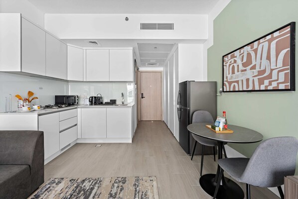 A modern kitchen with white cabinets, a dining area with a round table and chairs, and a living room with a sofa.