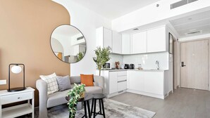 Ein modernes Wohnzimmer mit grauem Sofa, einem runden Spiegel, einem kleinen Tisch mit Hocker und einer Zimmerpflanze.