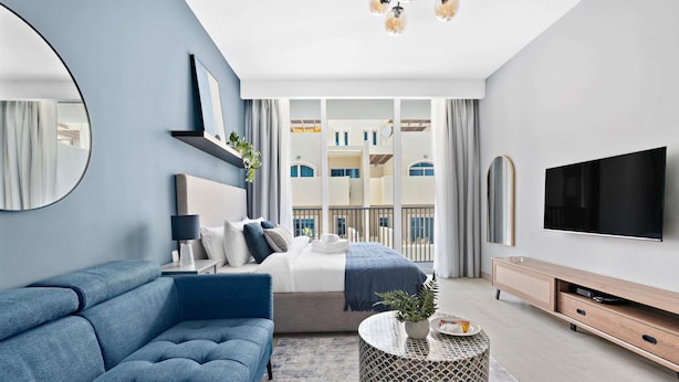 Ein modernes Schlafzimmer mit einer Couch, einem Bett, einem Fernseher und Blick auf einen Balkon.