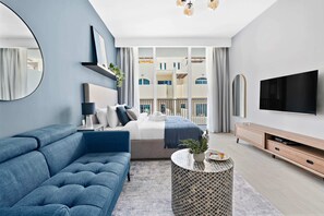 A modern bedroom with a sofa, bed, TV, and a balcony view.