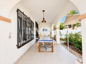 A covered patio area with a dining table and chairs, a black metal gate, and a hanging pendant light.