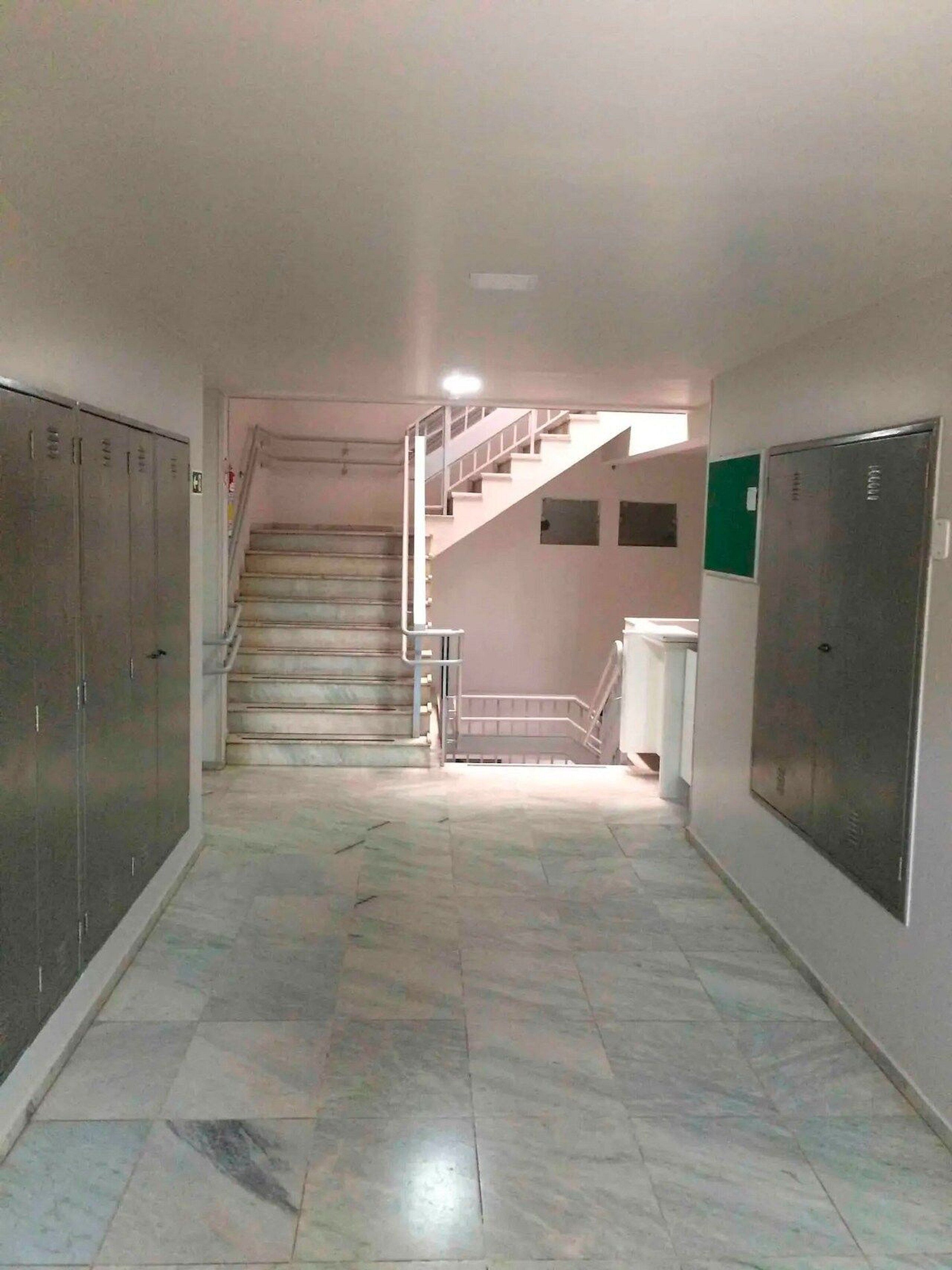 Un pasillo con taquillas, una escalera y piso de baldosas.