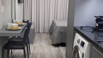 Una camera d'albergo compatta con zona pranzo, lavatrice e letto con copripiumino grigio.