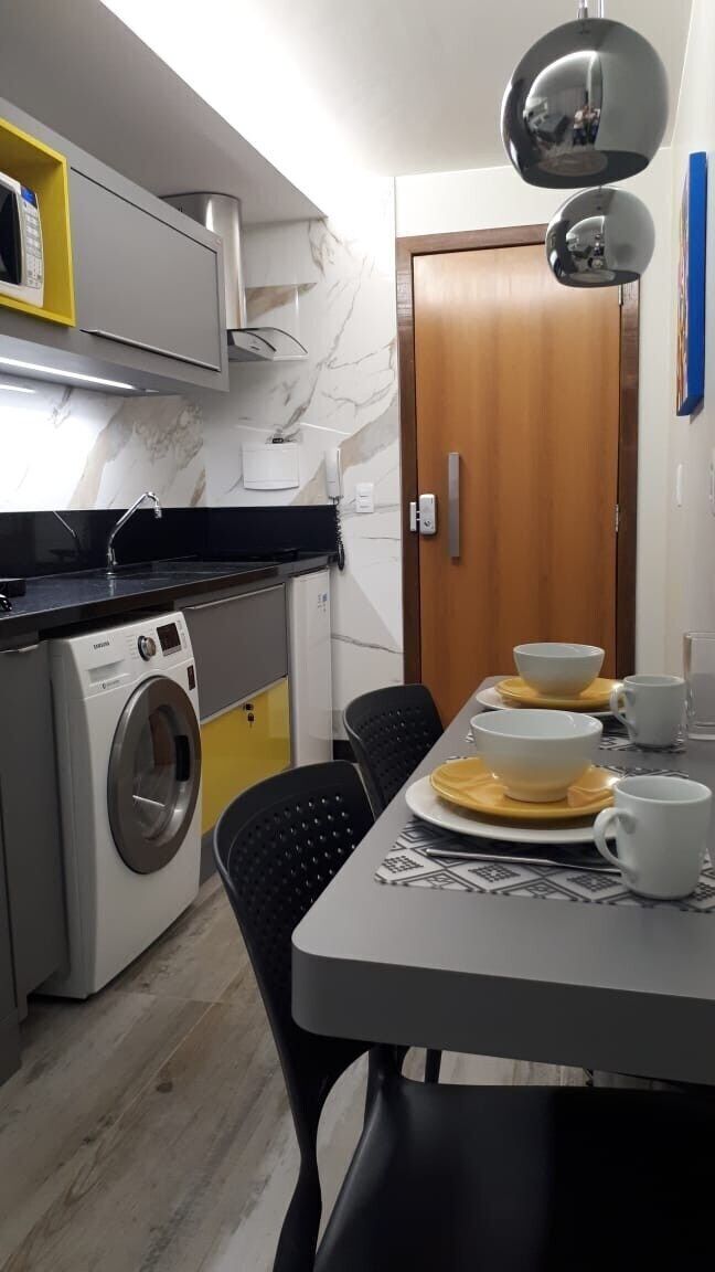 Cocina compacta con lavadora, microondas y comedor con mesa lista para dos.