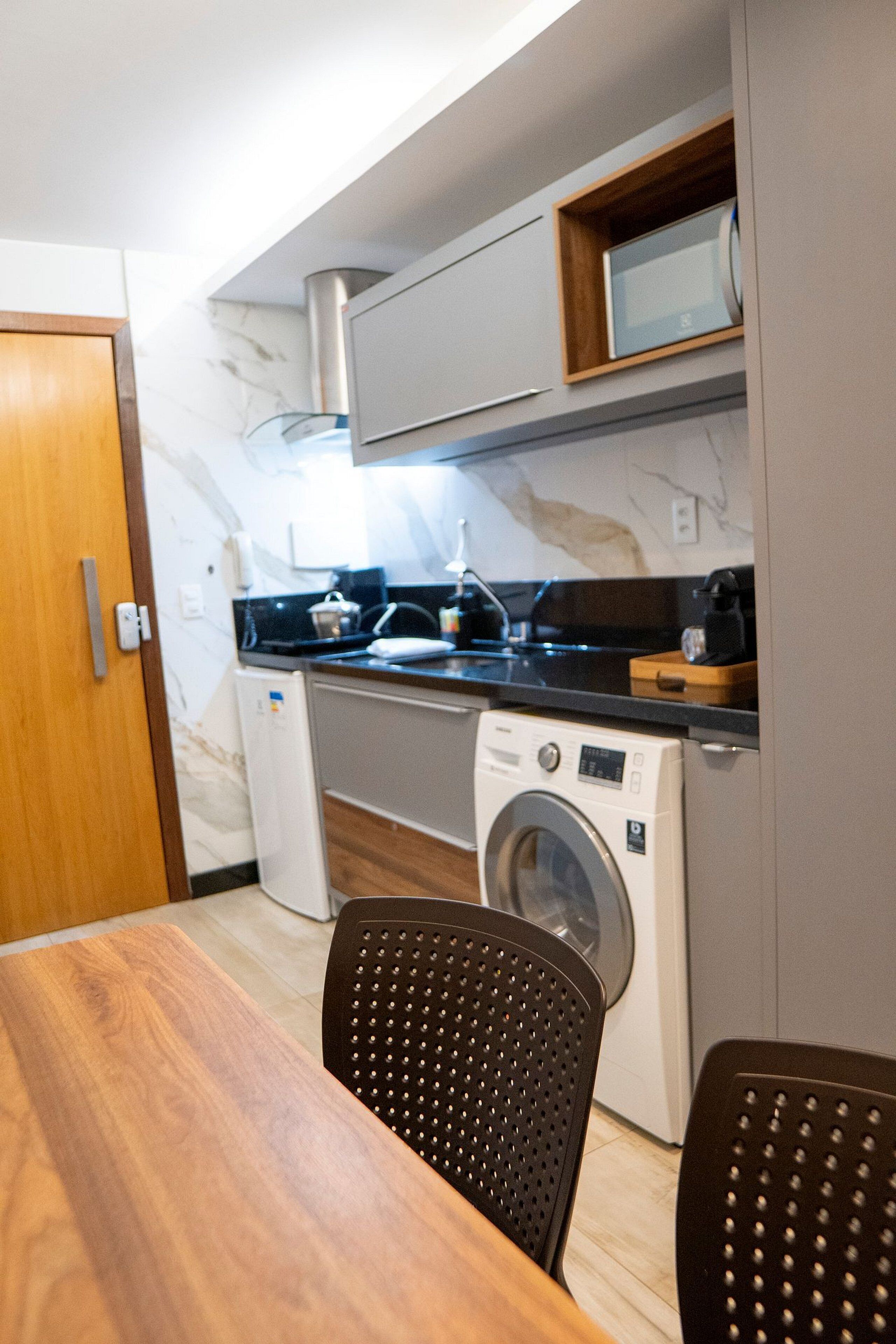 Une cuisine compacte équipée d’un lave-linge, d’un four à micro-ondes et d’une machine à café, le tout posé sur le plan de travail.