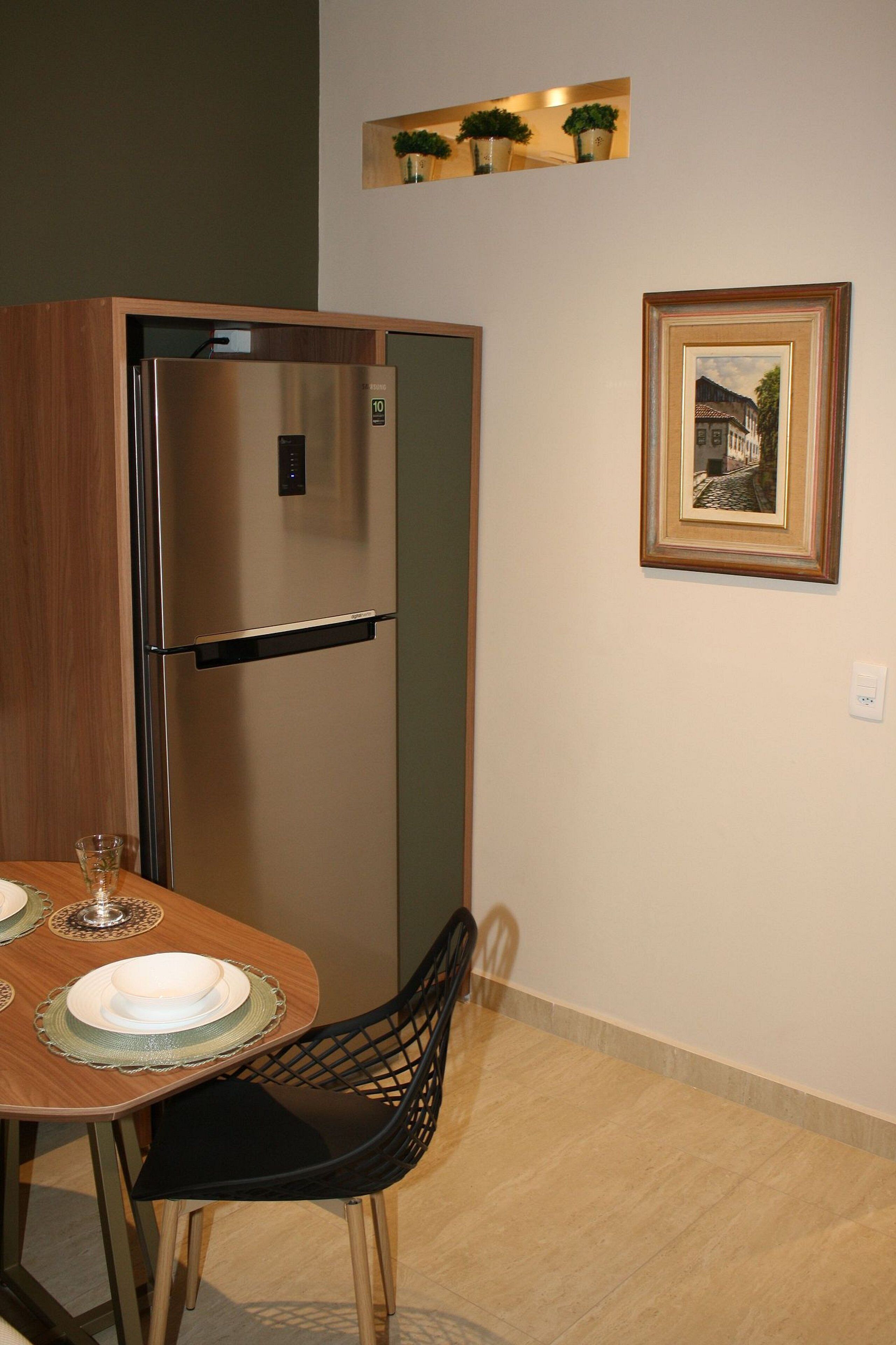 Cuina compacta amb frigorífic d'acer inoxidable integrat, taula de dinar amb cadires i una fotografia emmarcada a la paret.