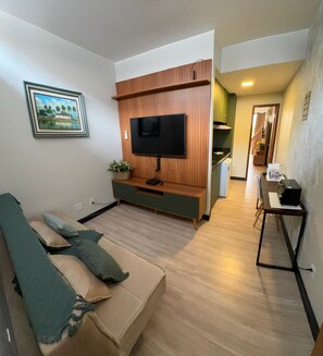 A living room with a sofa, a television, and a kitchen area in the background.