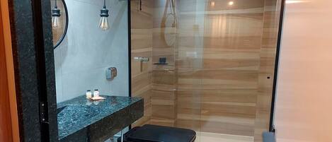 Un baño moderno con cabina de ducha de vidrio, lavamanos de mármol y inodoro negro.