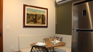 A small kitchenette with a stainless steel refrigerator, a dining table with chairs, and a painting on the wall.