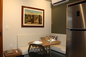 A small kitchenette with a stainless steel refrigerator, a dining table with chairs, and a painting on the wall.