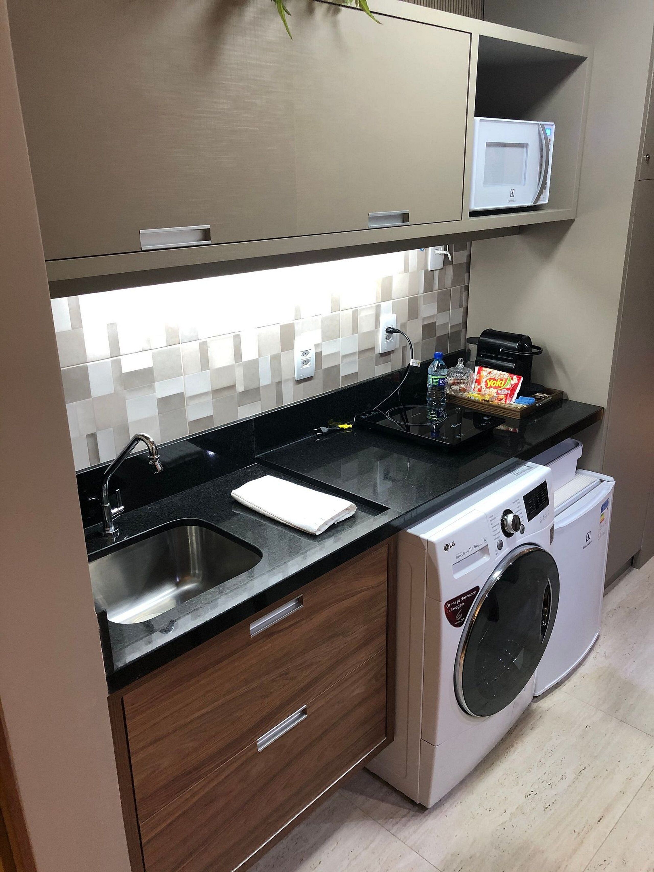 Una cocina compacta con lavadora integrada, microondas y lavamanos.