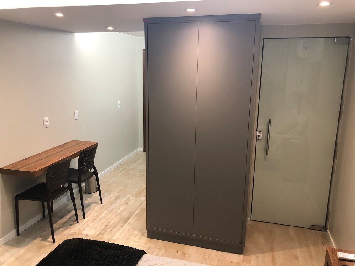 Ein Zimmer mit einem Holztisch, zwei Stühlen, einem dunklen Kleiderschrank und einer Glastür.
