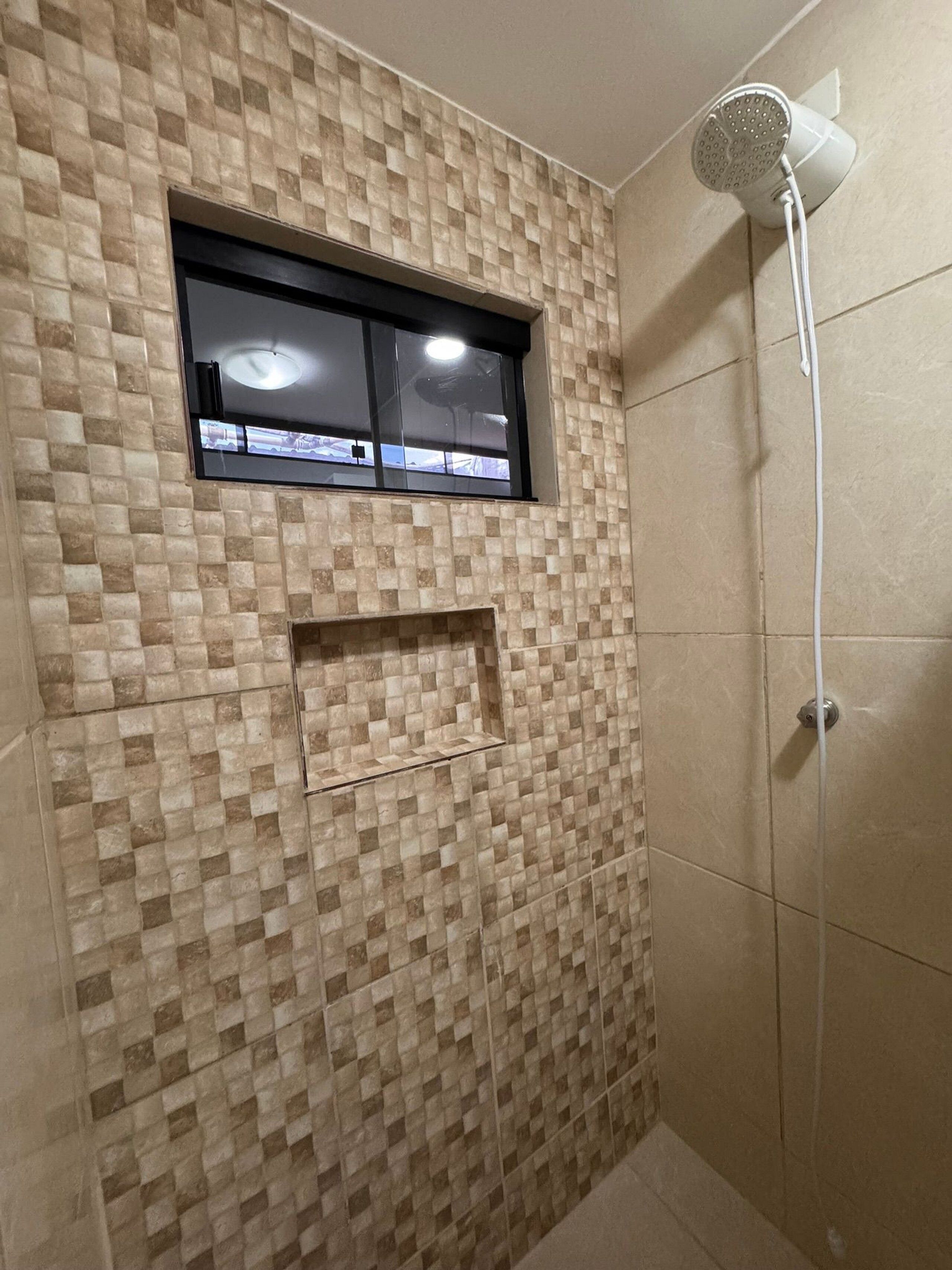 A shower with a handheld showerhead, a window with a black frame, and a tiled wall with a checkered pattern.