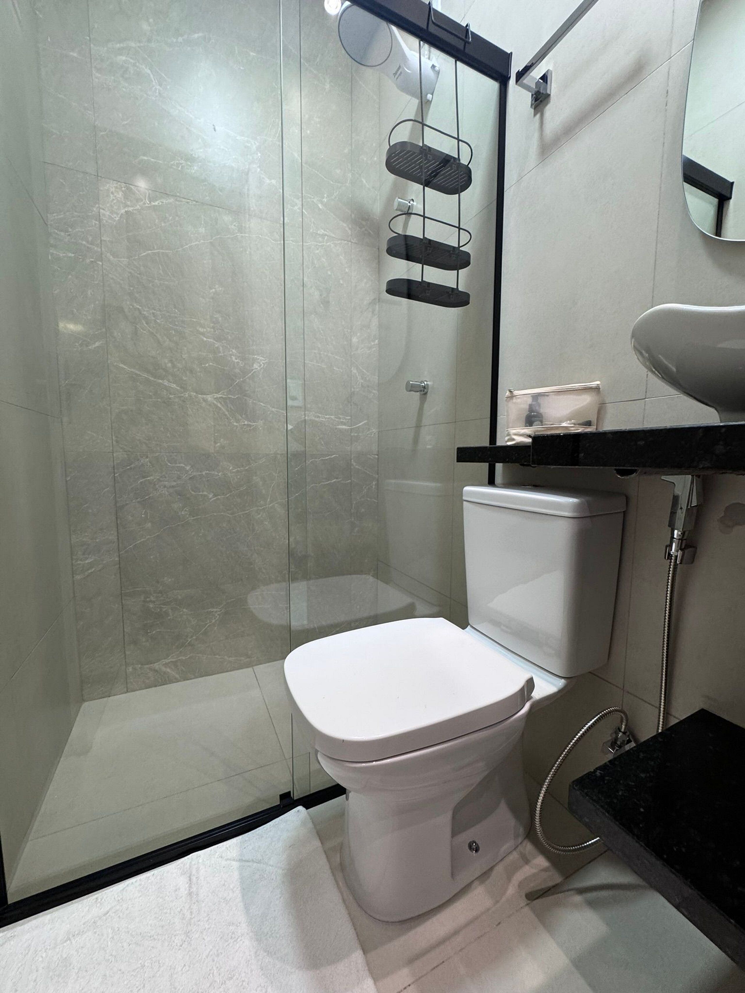 Une salle de bain moderne avec une douche à parois de verre, des toilettes blanches, un plan de toilette noir et un miroir.