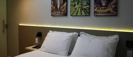 A hotel room with a bed, two white pillows, a nightstand with a phone, and three paintings on the wall.