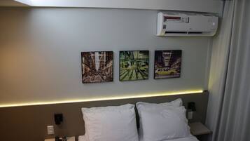 Une chambre d’hôtel avec un lit, des oreillers blancs, une table de chevet avec une télécommande et trois tableaux encadrés accrochés au mur.