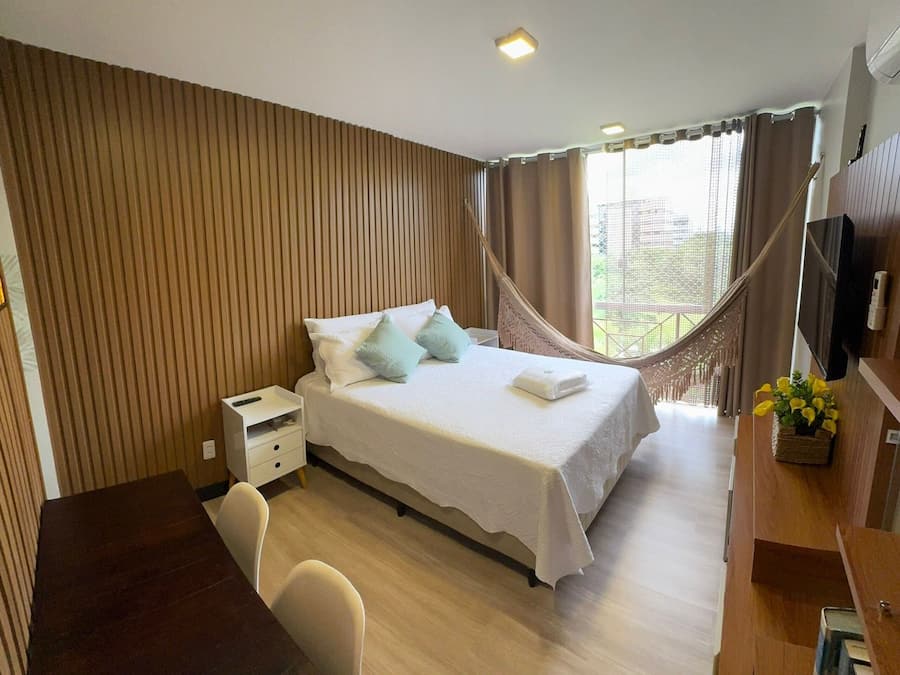 Ein Hotelzimmer mit Bett, Nachttisch, Stuhl, Schreibtisch, Fernseher und einer Hängematte.