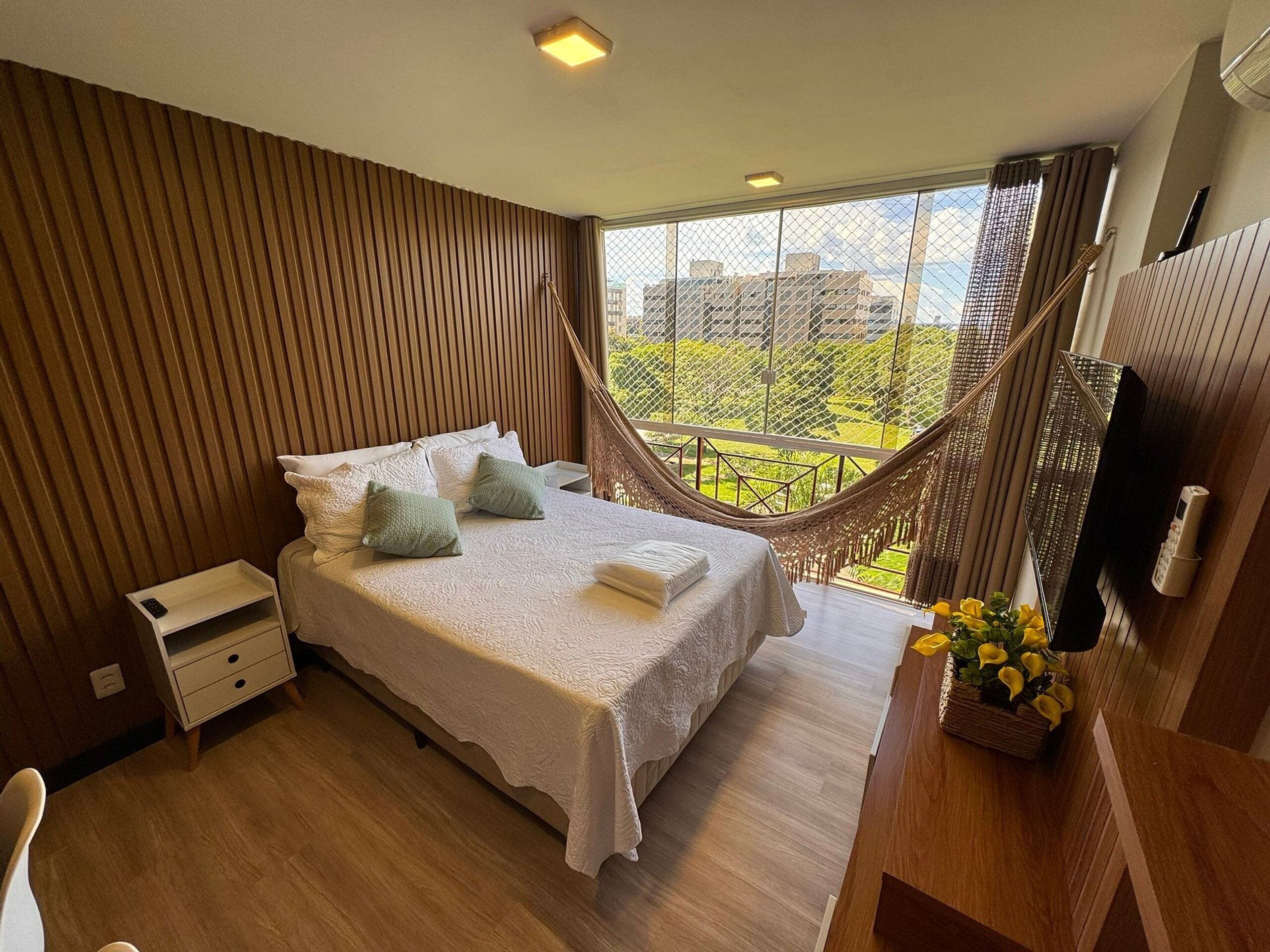 A bedroom with a bed, bedside table, and a view of the city through a window.
