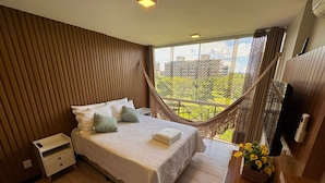 A bedroom with a bed, bedside table, and a view of the city through a window.