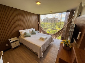 A bedroom with a bed, bedside table, and a view of the city through a window.