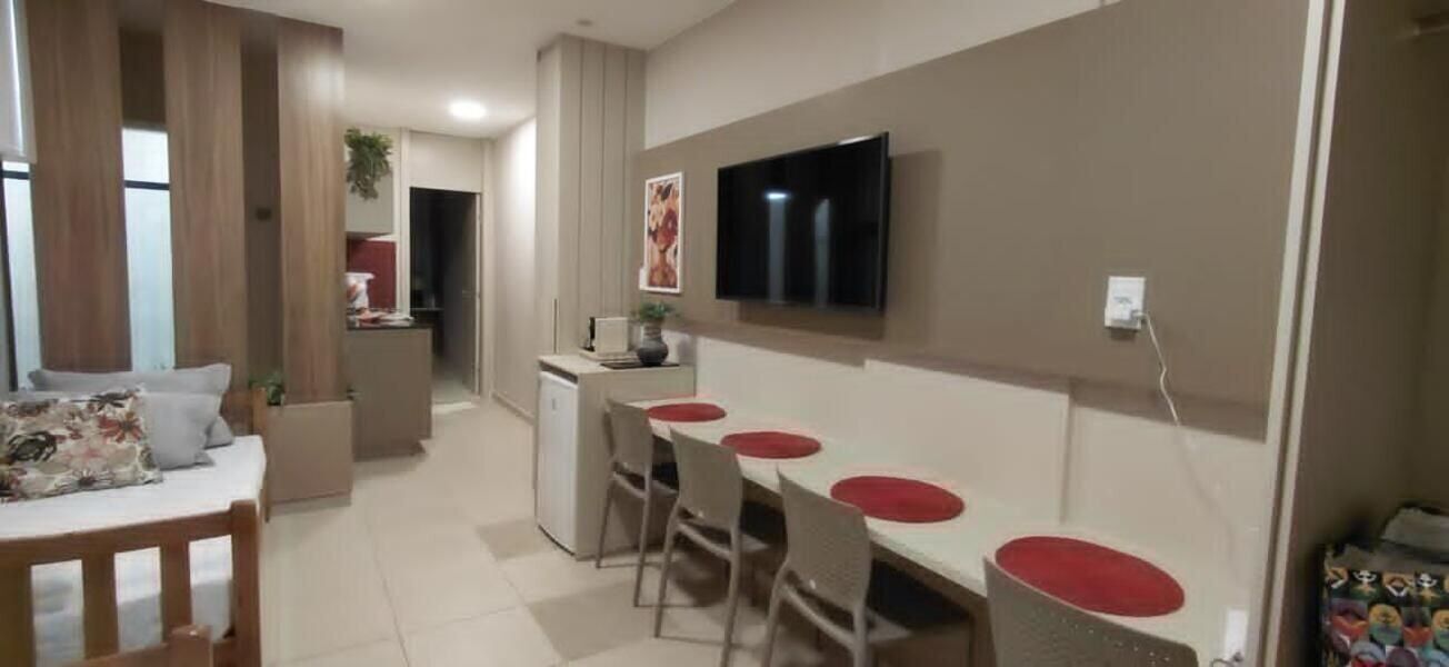 Een moderne woonkamer met een bank, een eettafel met stoelen, een aan de muur bevestigde televisie en een keuken in de achtergrond.