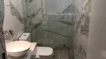 A modern bathroom with a glass-enclosed shower, a white sink, and a toilet.
