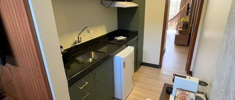 A compact kitchen with green cabinets, a white dishwasher, and a dining area with a table and chair.