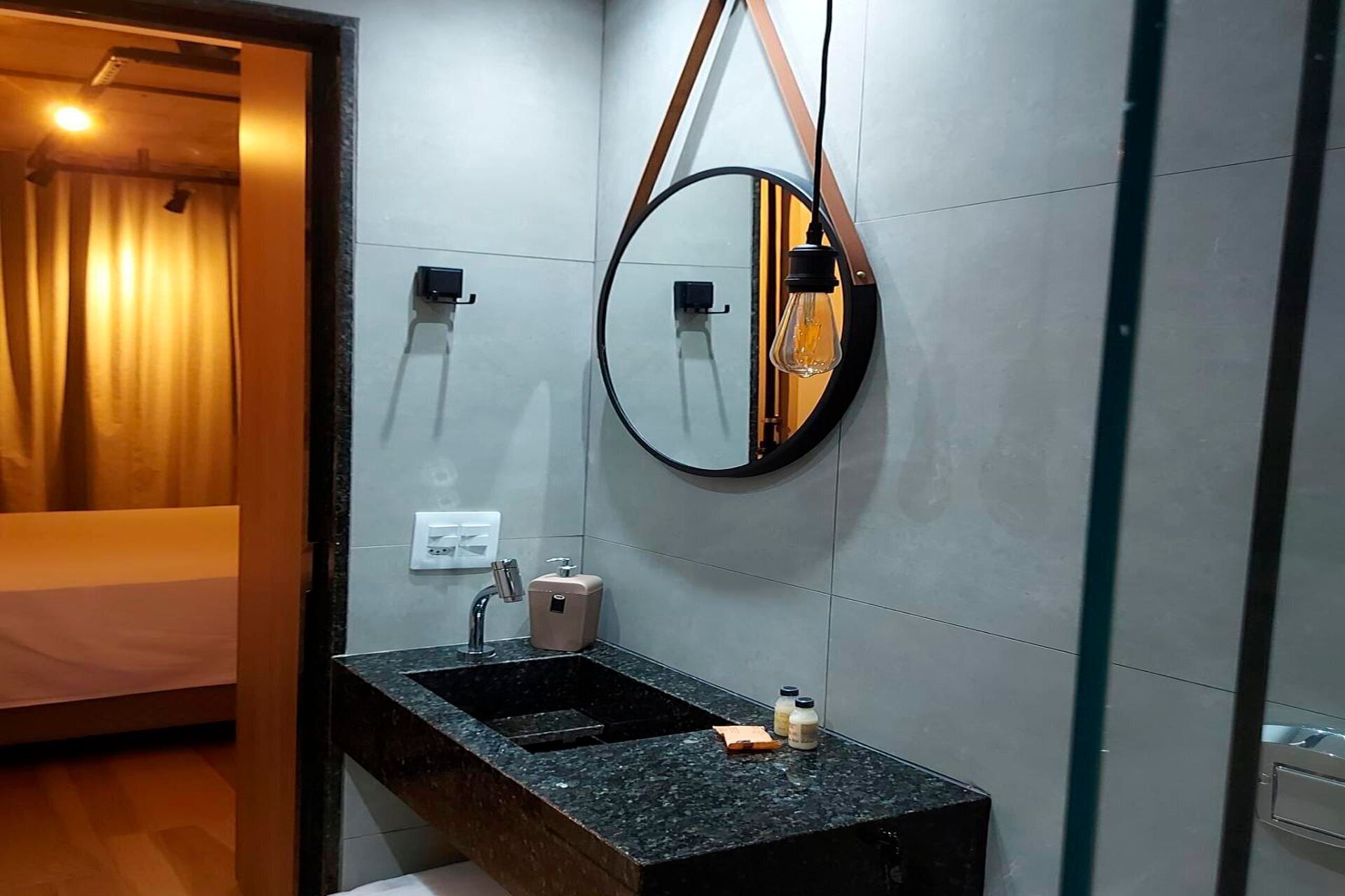 Uma casa de banho moderna com lavatório de granito, espelho redondo e porta-toalhas.