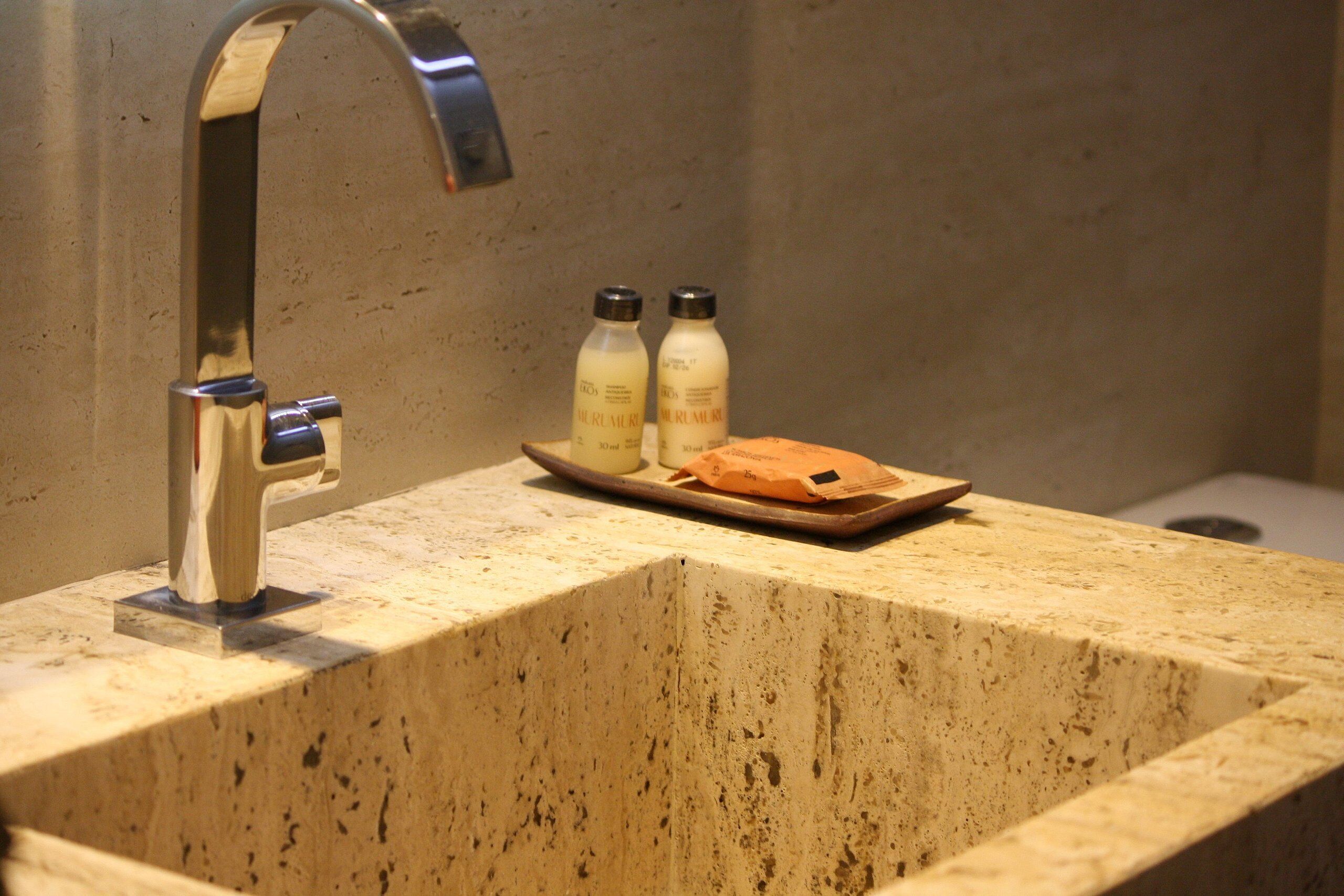 Une salle de bain avec un lavabo en marbre, un robinet moderne et deux flacons de savon liquide sur le comptoir.