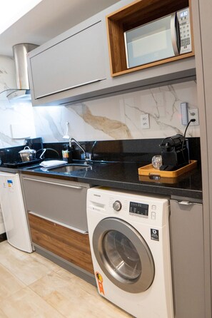 A compact kitchen with a microwave, coffee maker, and washing machine. - Flats Asa Norte CLN 110 bloco B (Brasília)