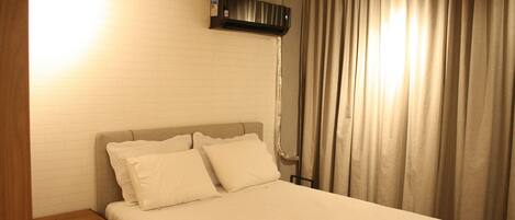Une chambre d’hôtel avec un lit, une table de chevet, un climatiseur fixé au mur et une fenêtre avec des rideaux.