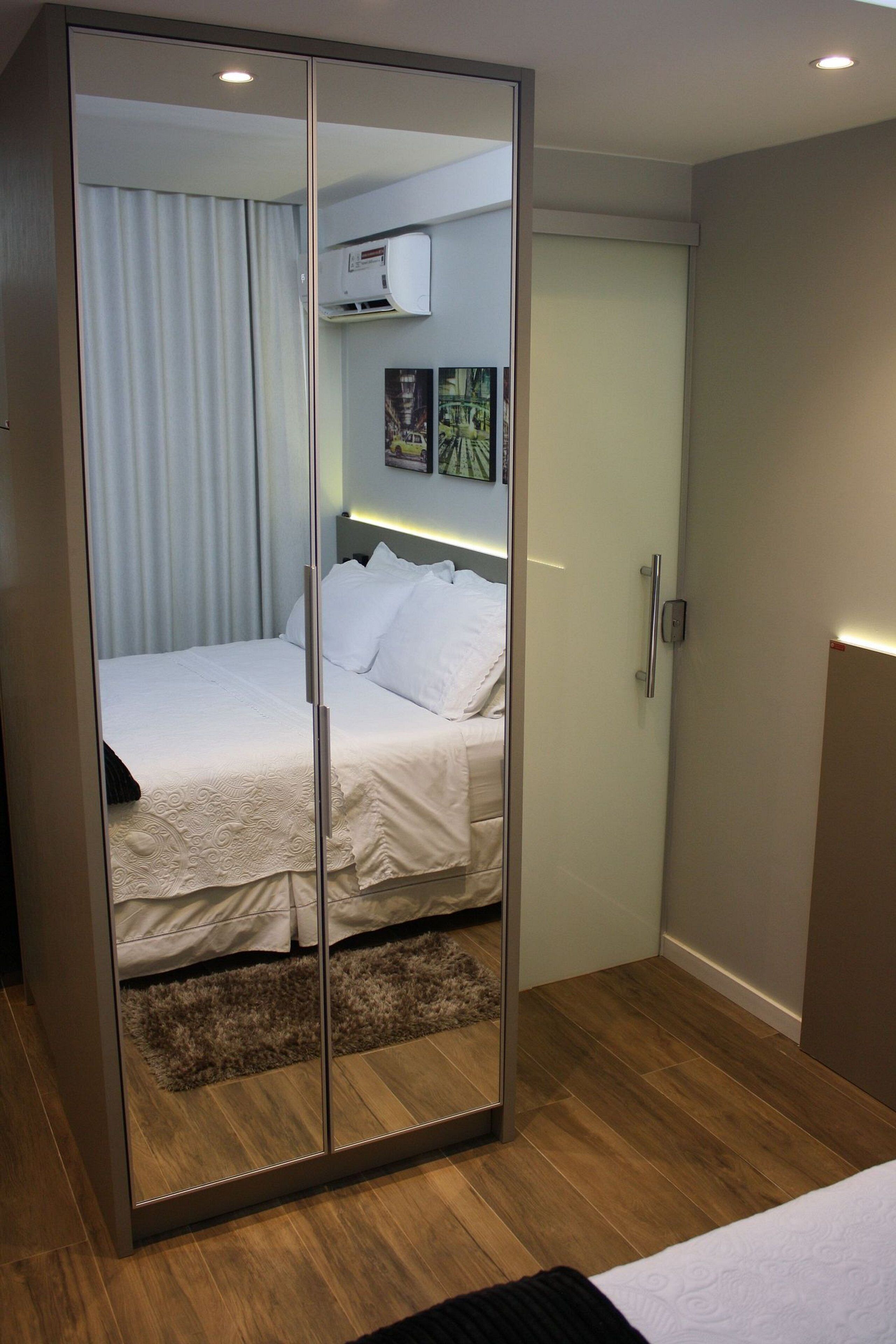 Un dormitorio con un armario espejado, una cama con ropa de cama blanca, suelo de madera y aire acondicionado instalado en el techo.