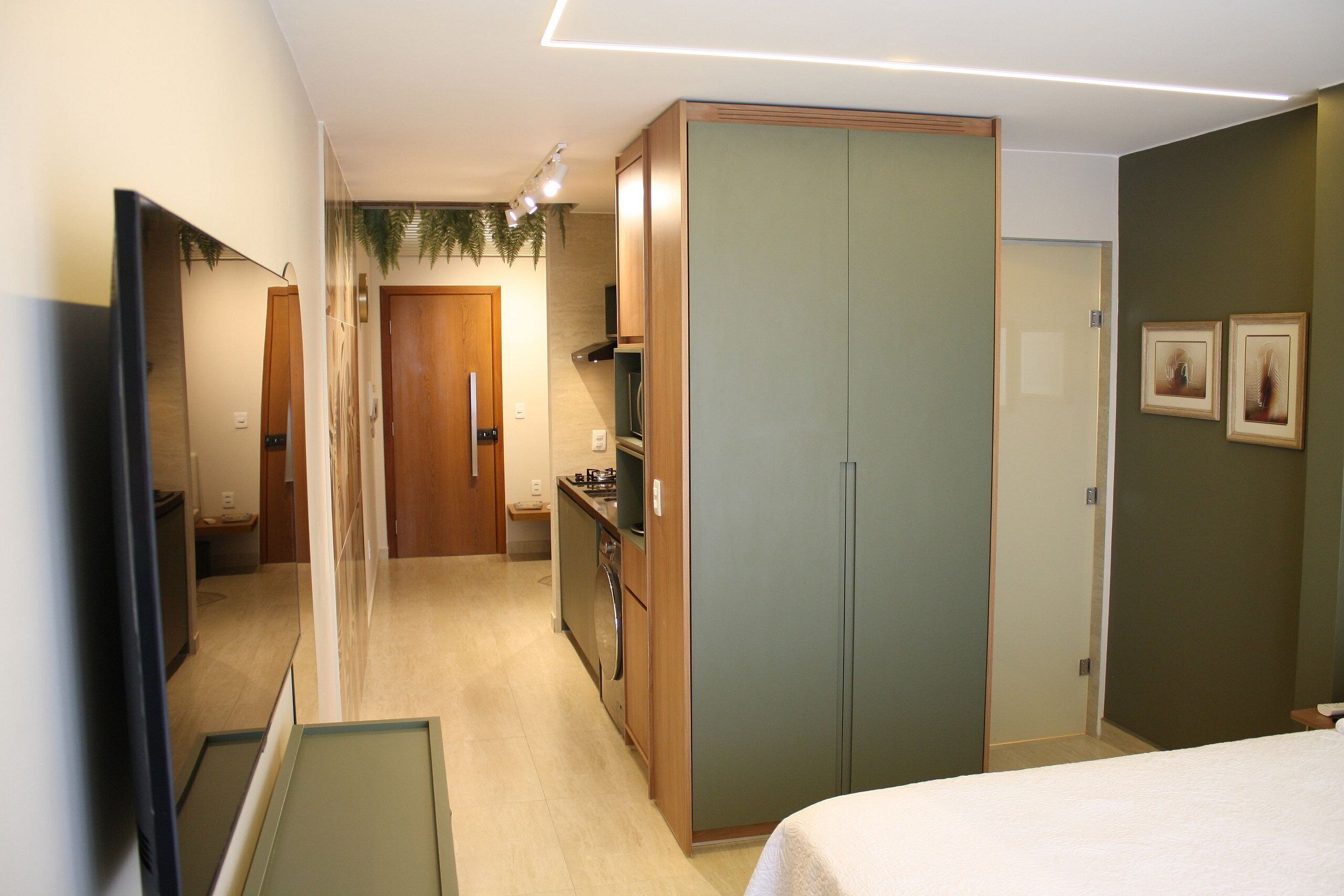 A hotel room with a bed, a wardrobe, a mirror, a small kitchenette, and a door leading to another room.