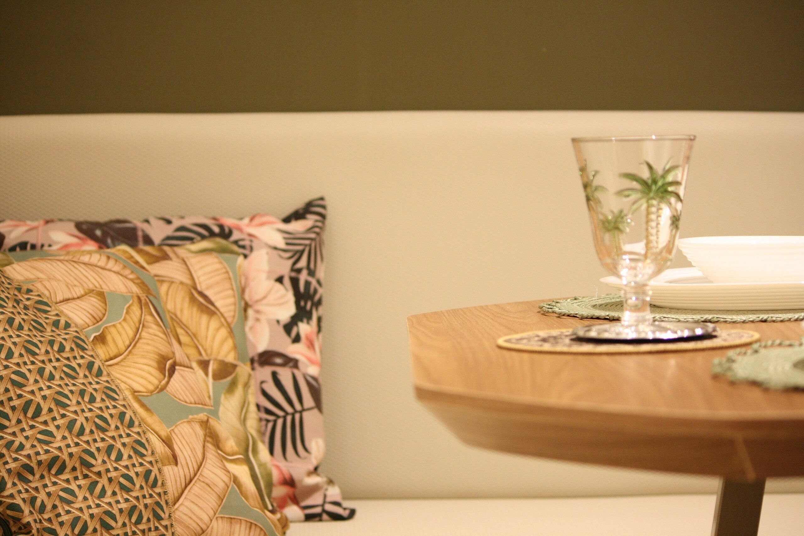 Una mesa de comedor con una copa, platos y un cojín decorativo.
