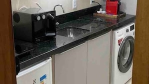 A compact kitchen with a microwave, a small refrigerator, a washing machine, and a sink.