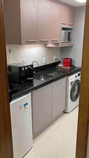 A compact kitchen with a microwave, a small refrigerator, a washing machine, and a sink.