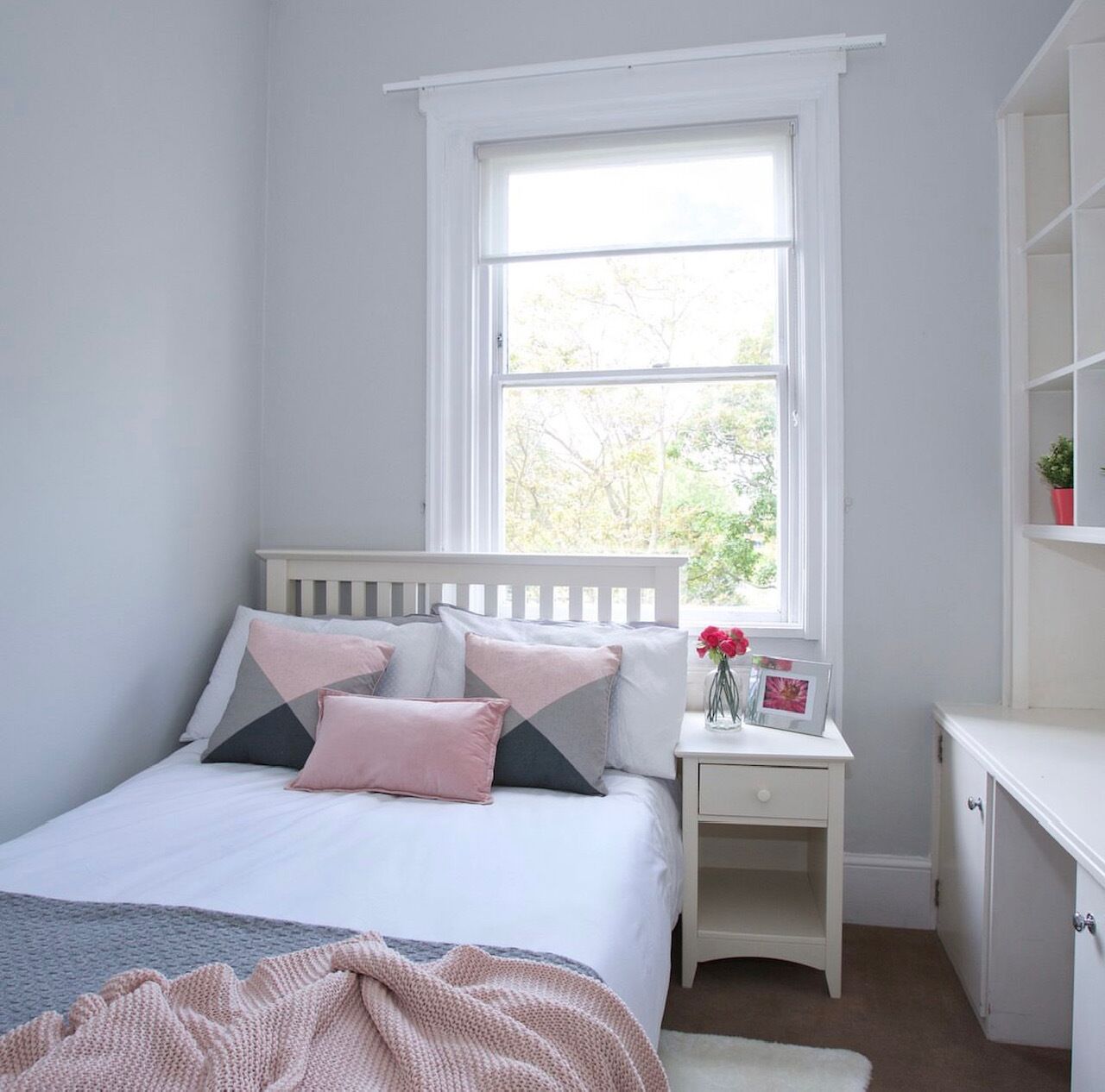Un dormitorio con cama, mesita de noche, cómoda y ventana con vista a árboles.