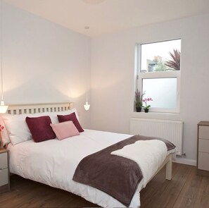Relax in this serene bedroom with a large bed, white headboard, and cozy throw blanket.
