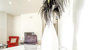Un salón moderno con un jarrón blanco grande, un sillón rojo, un sillón morado y una mesita auxiliar pequeña.