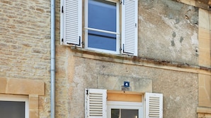 Un edificio con fachada de piedra, puerta de madera con contraventanas y una ventana pequeña con contraventanas.