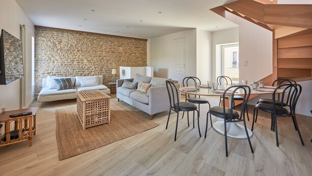 Una sala moderna con pared de piedra, un sofá, una mesa de centro y un comedor con sillas y una mesa.