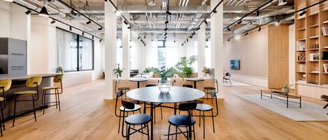 Una amplia sala de conferencias con una mesa redonda, varias sillas y un techo moderno con conductos y luminarias a la vista.